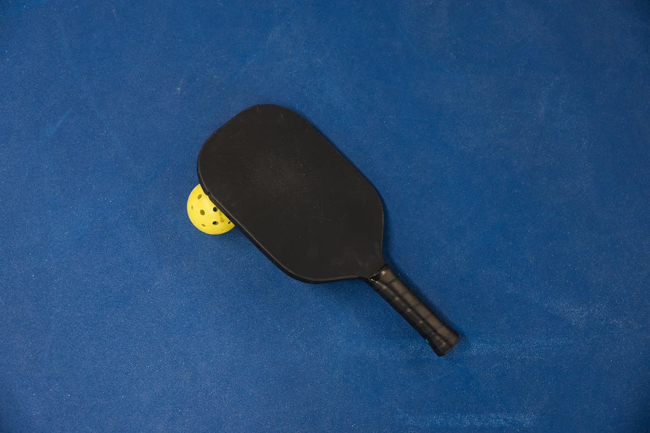 our-journey-03 A pickleball paddle and ball on a textured blue surface, showcasing sports equipment.